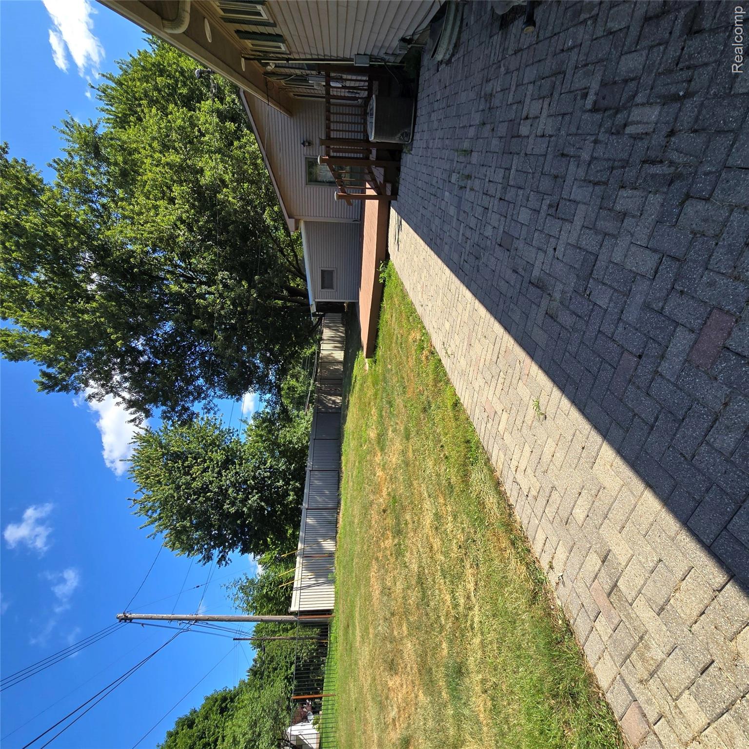 311 Nevada Avenue Rochester, MI 48309 - Photo 9 of 70 Paved brick walkway leading to a wood deck with railings, an air conditioning unit, and a detached shed