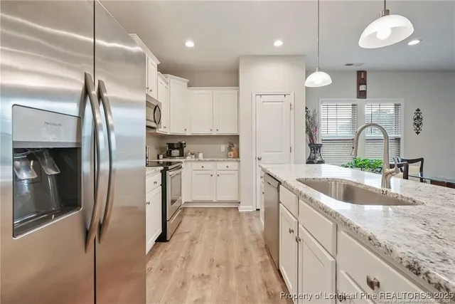 a kitchen with stainless steel appliances granite countertop a refrigerator a sink and white cabinets