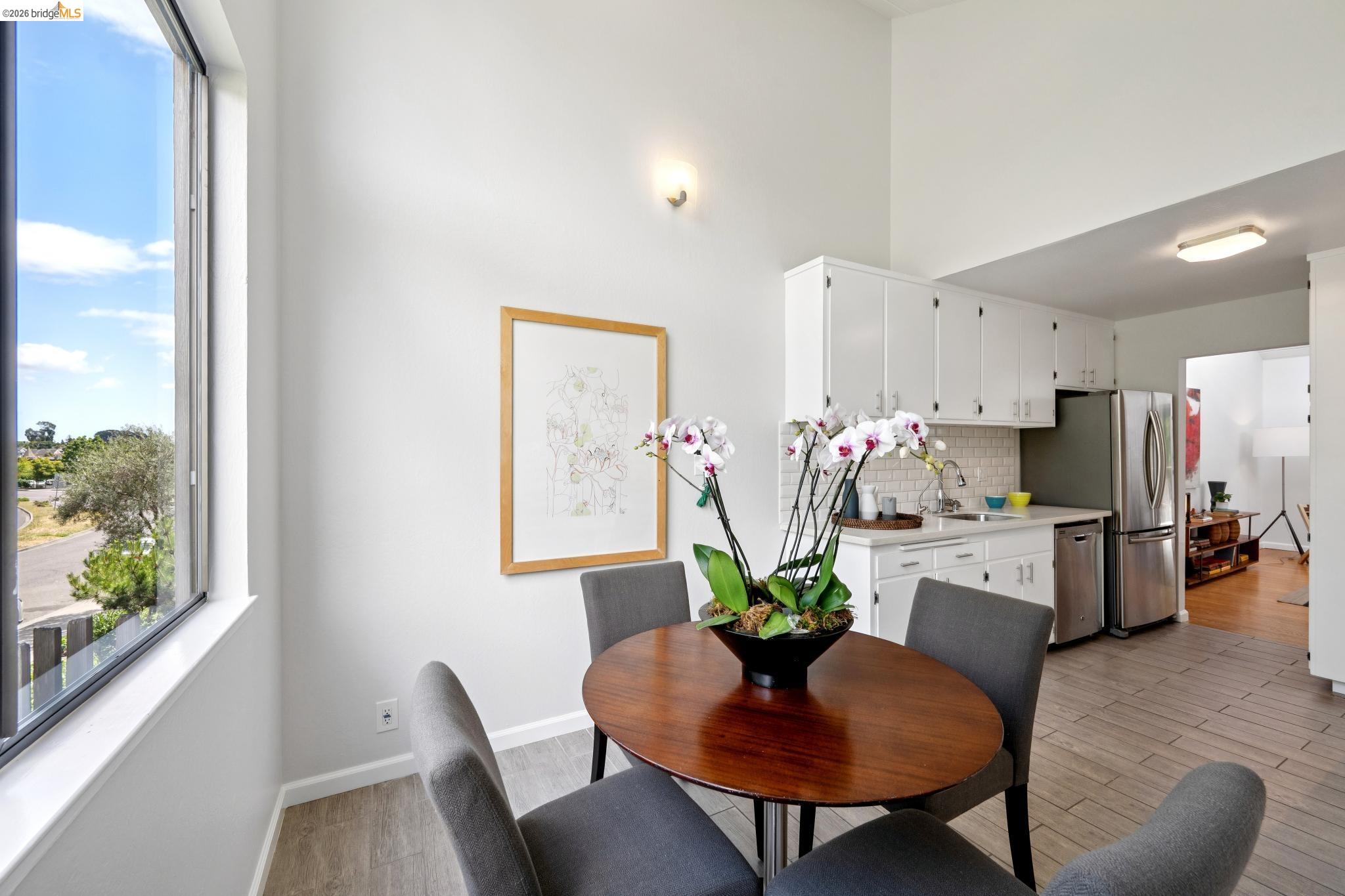 1340 Henry Street Berkeley, CA 94709 - Photo 27 of 52 Kitchen and dining area featuring a vaulted ceiling, wood-finish flooring, white cabinetry, stainless steel appliances, and a window with exterior views