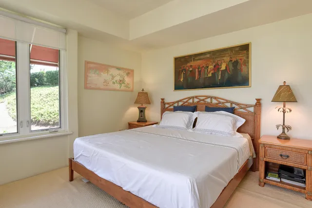 a bedroom with a bed and a lamp on dresser next to a window