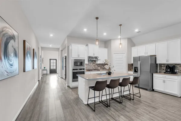 a kitchen with stainless steel appliances a refrigerator a stove top oven a sink dishwasher and a dining table with wooden floor
