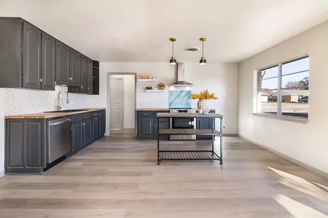a living room with stainless steel appliances kitchen island granite countertop a sink dishwasher and a stove with wooden floor