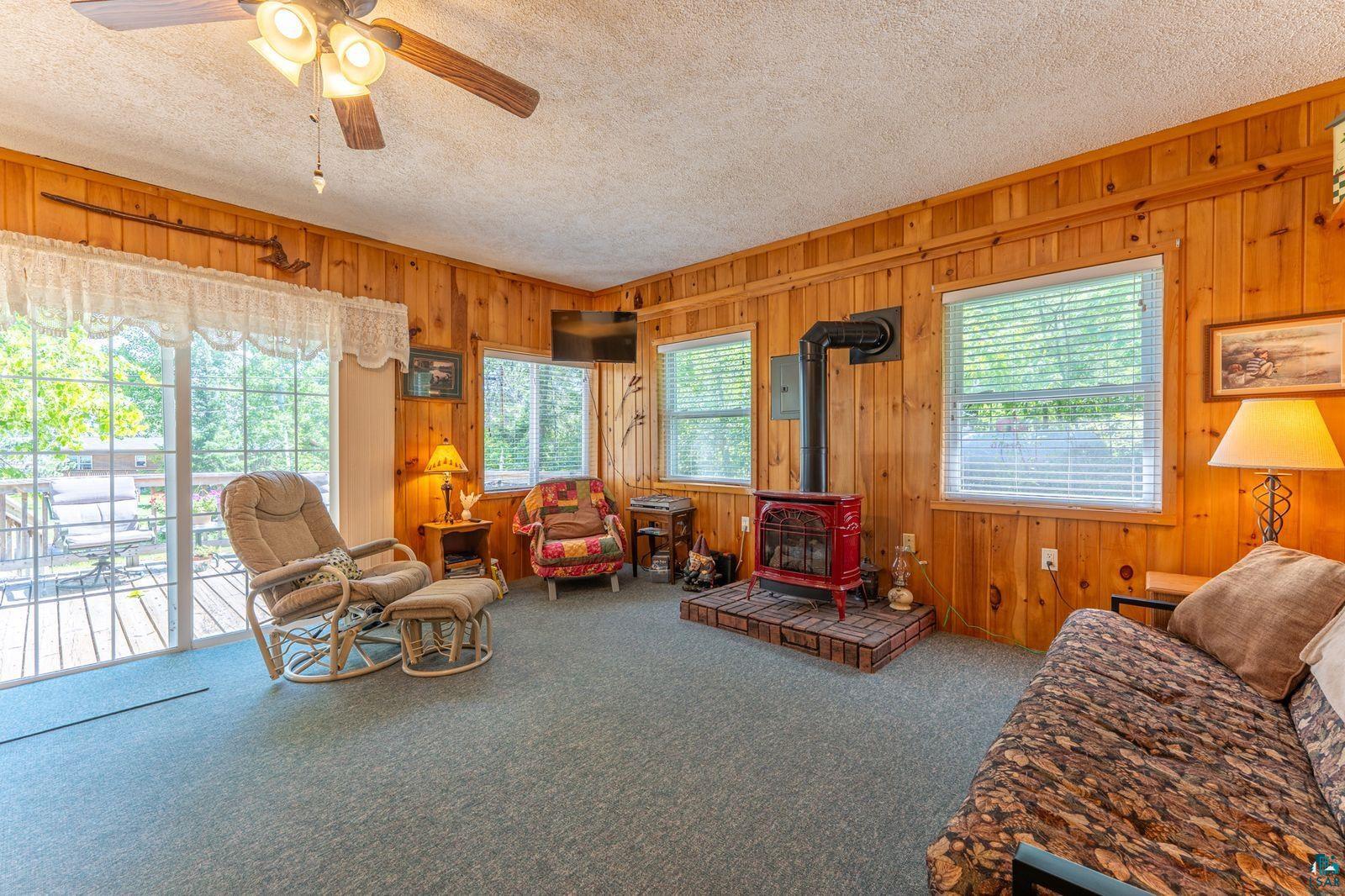 3609 Fectos Road Tower, MN 55790 - Photo 5 of 24 Carpeted living room featuring a wood stove, ceiling fan, wood walls, a textured ceiling, and electric panel