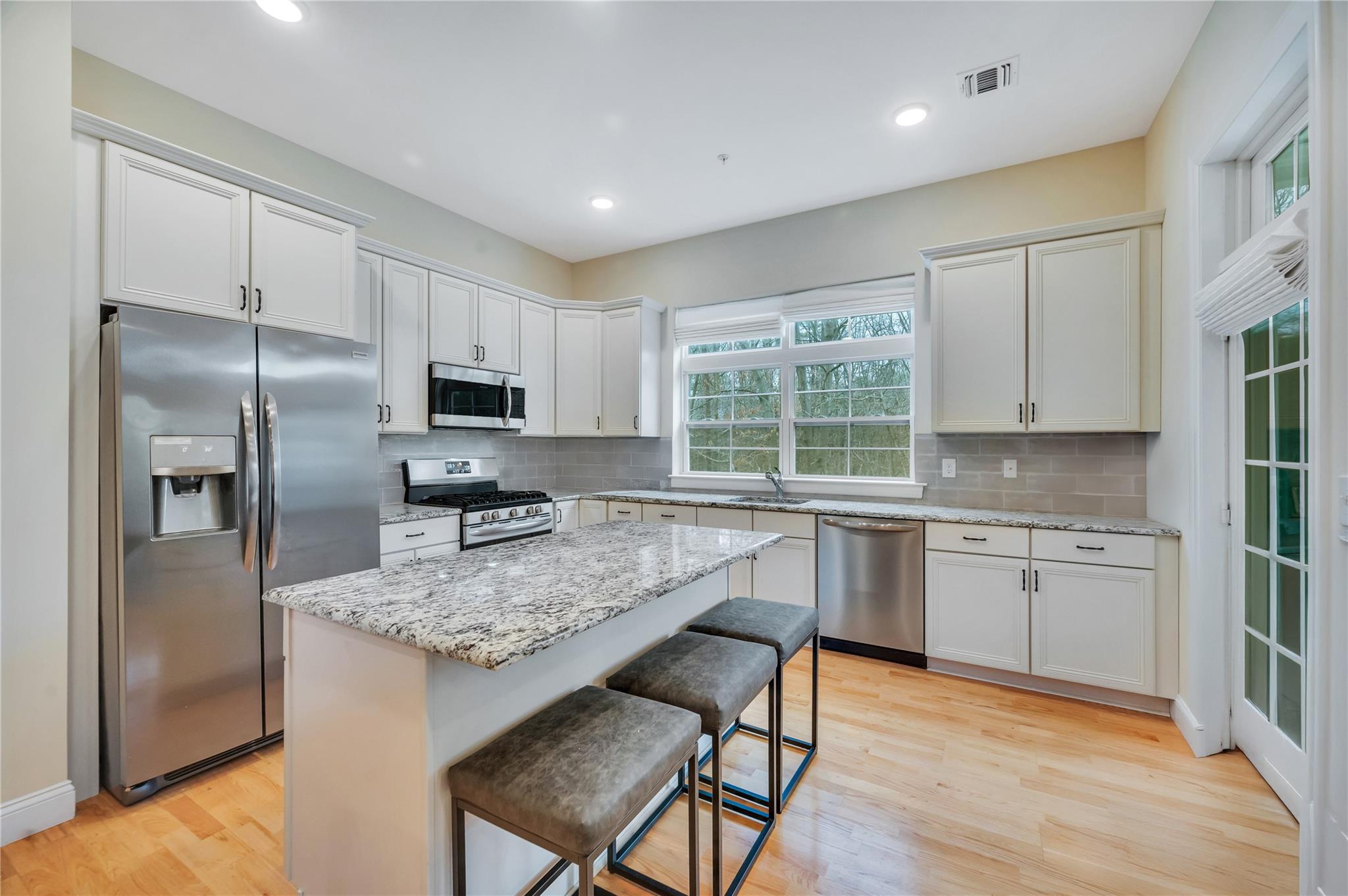 a kitchen with granite countertop stainless steel appliances a sink stove refrigerator and window