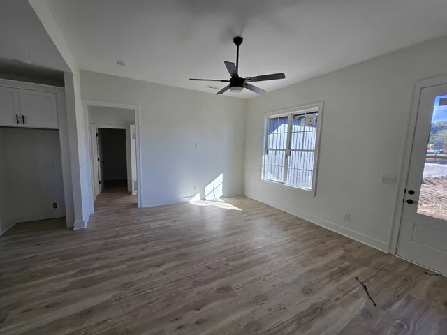 an empty room with wooden floor chandelier fan and windows