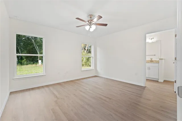 an empty room with wooden floor a ceiling fan and windows