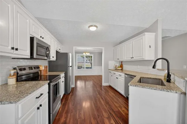 a kitchen with granite countertop a stove top oven a sink dishwasher and a refrigerator with wooden floor