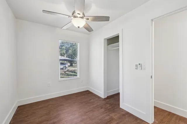 an empty room with wooden floor chandelier fan and windows