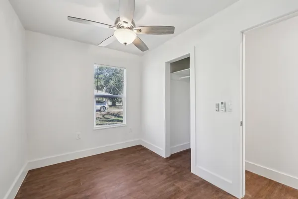 an empty room with wooden floor chandelier fan and windows