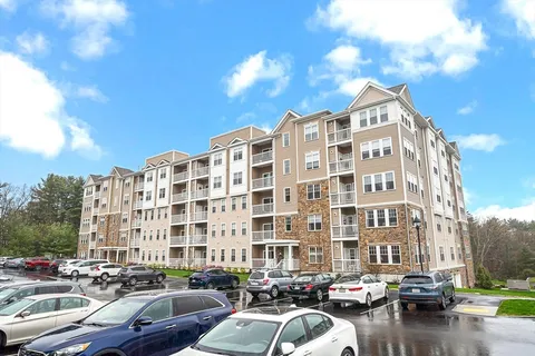 a front view of a building with lot of cars and trees