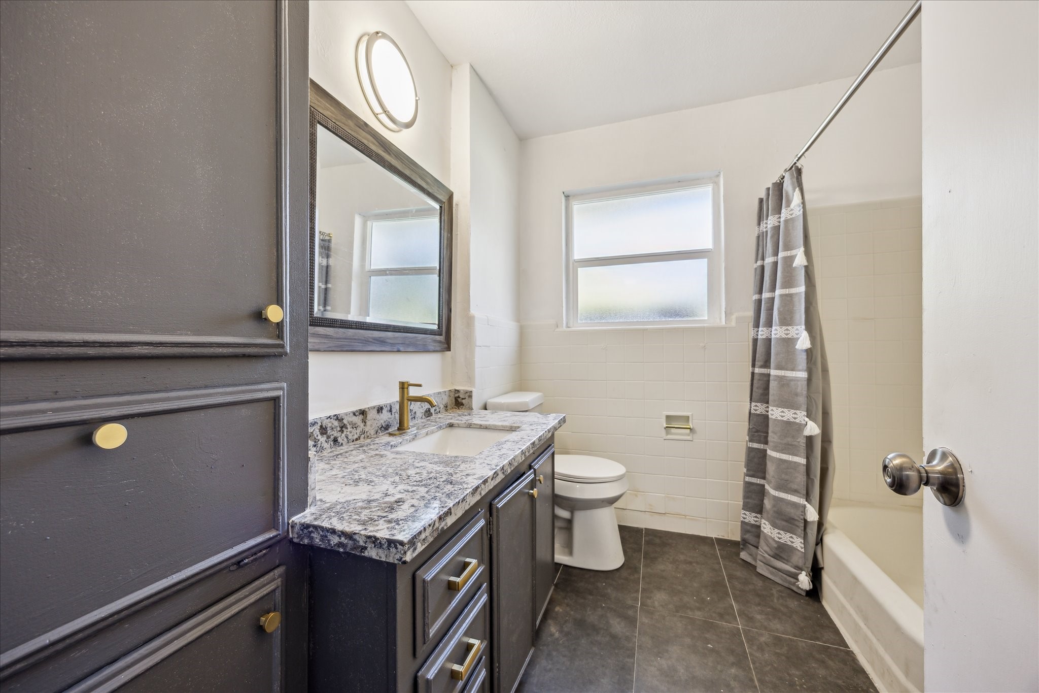 5419 Beechnut Street Houston, TX 77096 - Photo 14 of 28 Updated bathroom with granite vanity, framed mirror, modern fixtures, built-in storage, and tub/shower combo with tile surround.