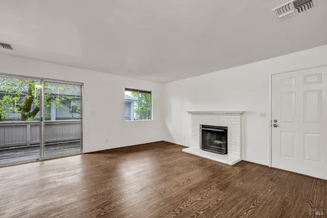 an empty room with wooden floor fireplace and windows