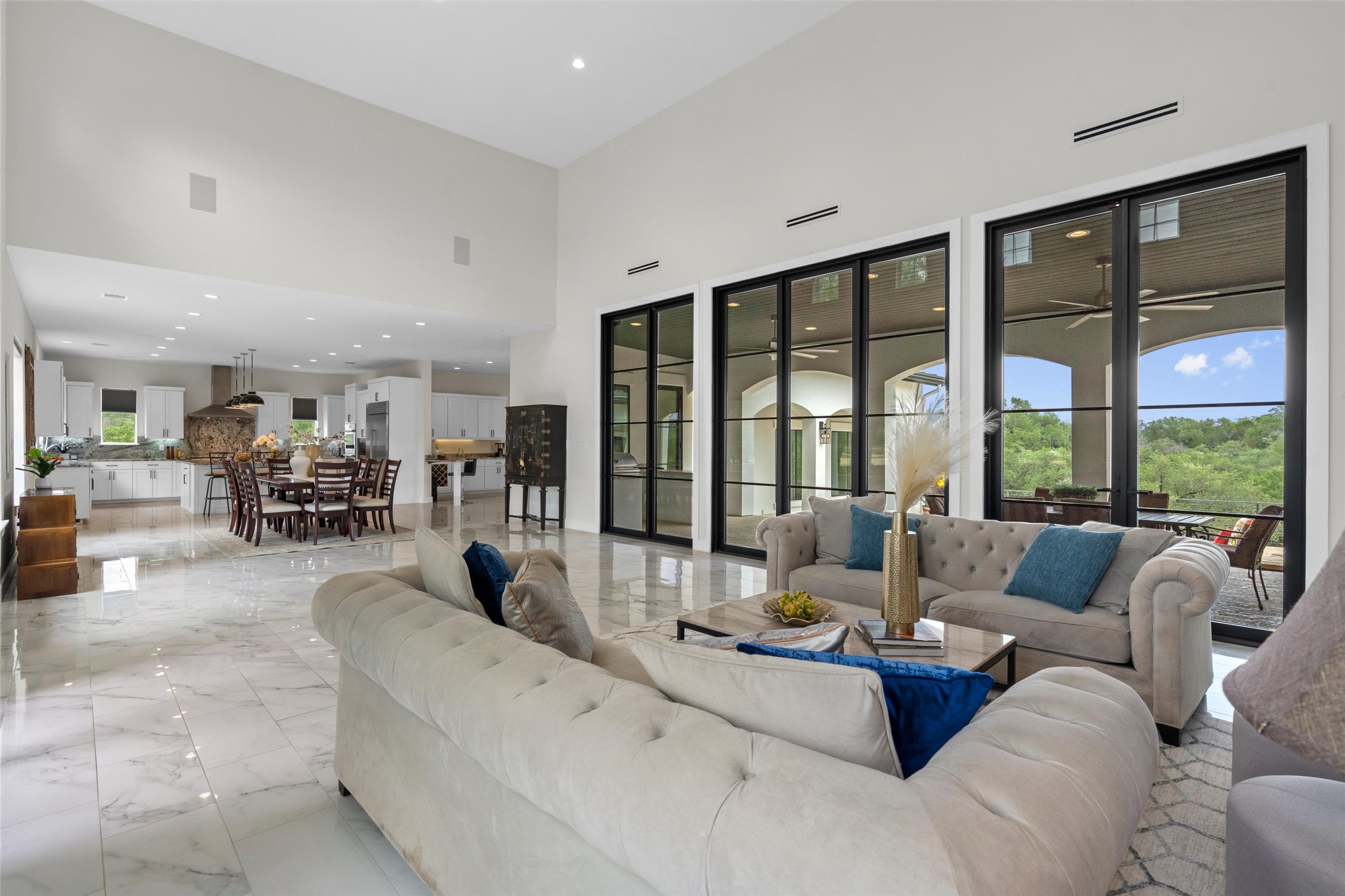 1805 Performer Road Spicewood, TX 78669 - Photo 5 of 40 Spacious living area with high ceilings, large format marble-look flooring, and a wall of black-framed glass doors
