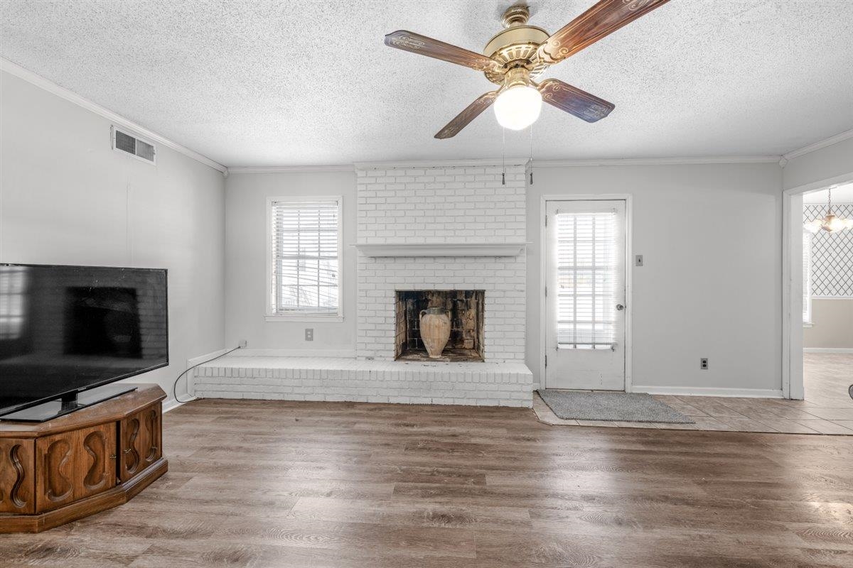 436 Sterling Drive Collierville, TN 38017 - Photo 23 of 40 Unfurnished living room featuring a textured ceiling, a fireplace, wood finished floors, crown molding, and ceiling fan