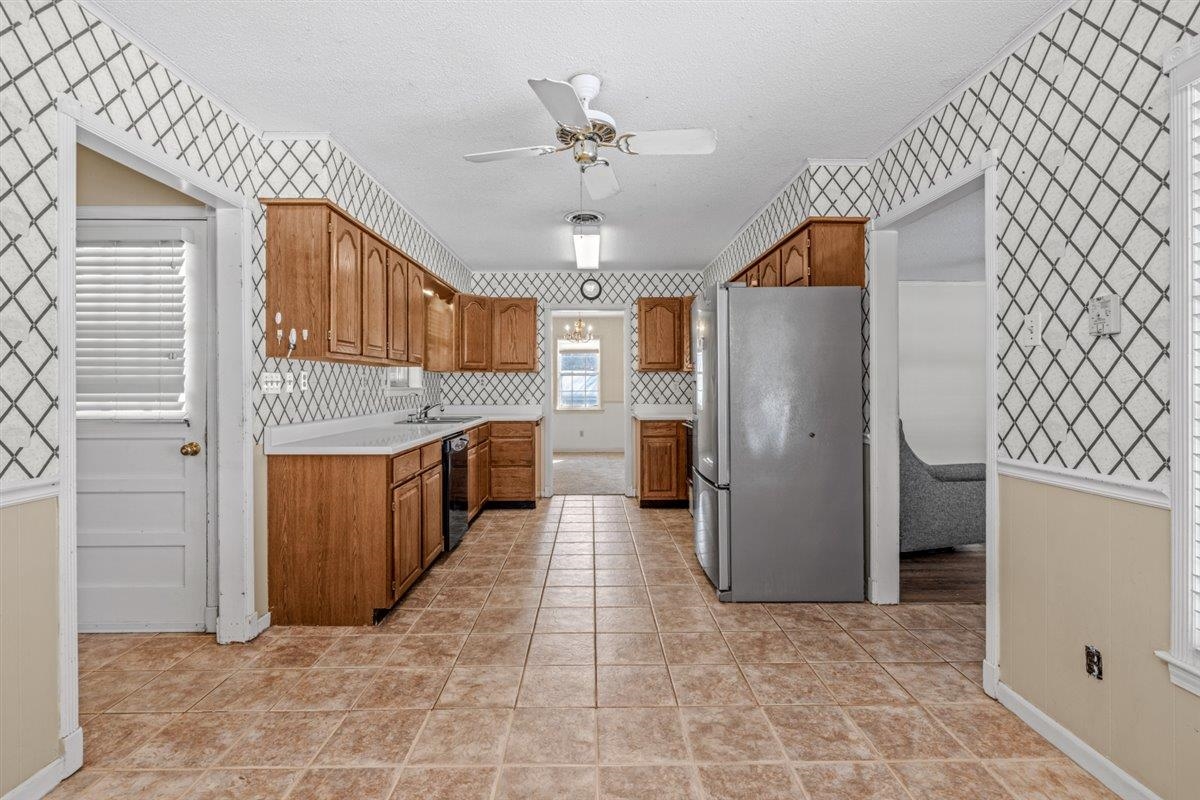436 Sterling Drive Collierville, TN 38017 - Photo 29 of 40 Kitchen featuring brown cabinetry, light countertops, wallpapered walls, freestanding refrigerator, and a textured ceiling