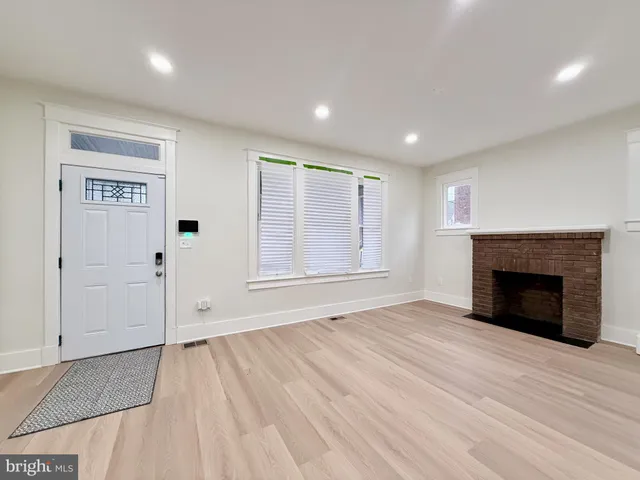 a view of an empty room with wooden floor fireplace and a window
