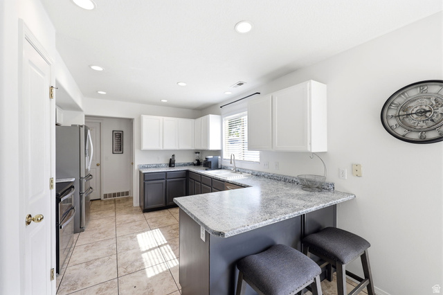 5485 Heather Way Tooele, UT 84074 - Photo 21 of 41 Kitchen featuring a peninsula with countertop seating, white upper cabinetry, dark lower cabinetry, stainless steel appliances, recessed lighting, and tile flooring