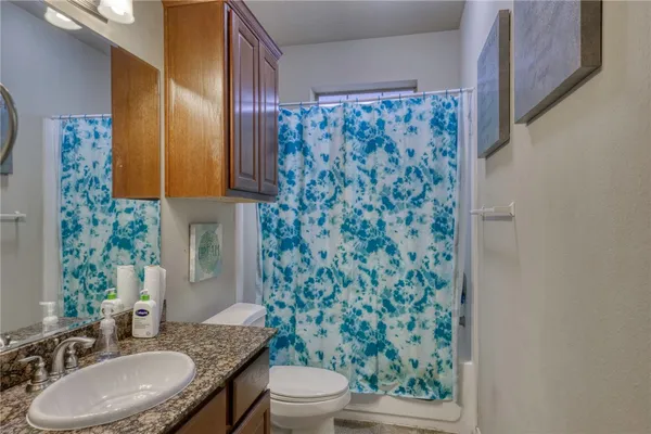 a bathroom with a granite countertop toilet a sink a mirror and a shower