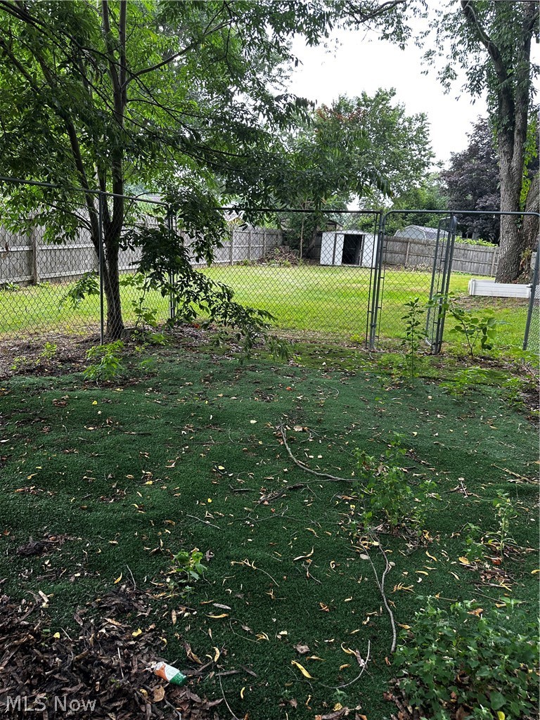 198 Park Road Painesville, OH 44077 - Photo 14 of 31 Fenced backyard featuring a chain-link perimeter, mature trees, a wooden privacy fence, and a white storage shed