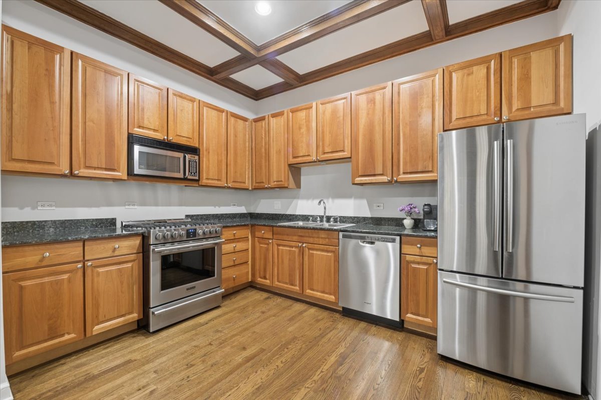 4028 North Sheridan Road, Unit 1R Chicago, IL 60613 - Photo 4 of 15 a kitchen with granite countertop wooden floors white stainless steel appliances and center island