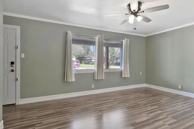 an empty room with wooden floor fan and windows
