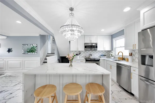 a kitchen with furniture a chandelier stainless steel appliances and cabinets