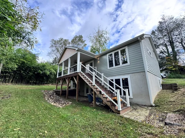 a view of a small house in front of a yard with plants and large tree