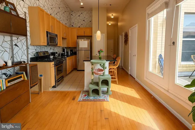 a living room with stainless steel appliances furniture a rug kitchen view and a large window