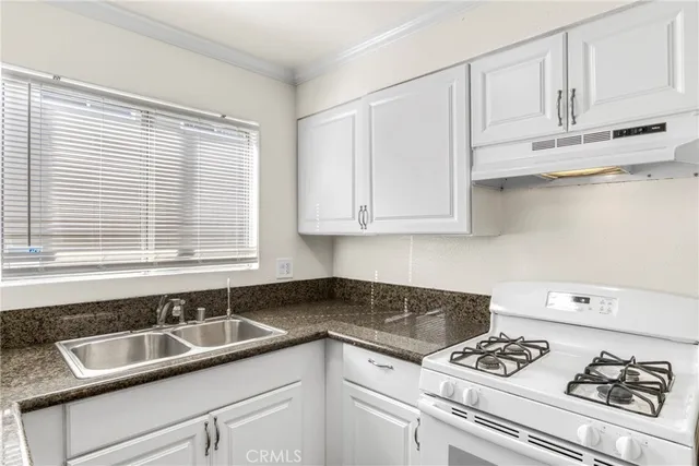 a kitchen with granite countertop a sink white cabinets and a stove