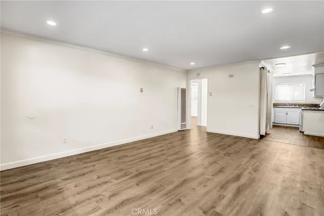 an empty room with wooden floor and a kitchen