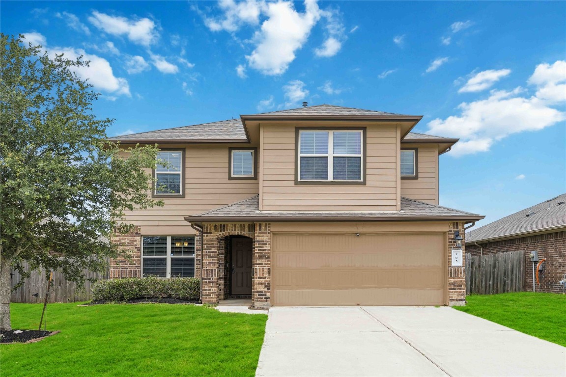 Welcome to 703 Autumn Flats Way. The covered front entryway features a classic brick archway, providing a sheltered and stylish welcome for guests. Includes a wide concrete driveway leading to a two-car attached garage with a clean, coordinated finish