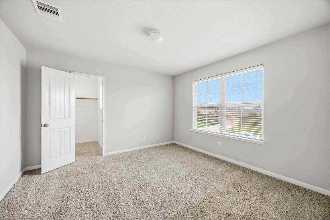 703 Autumn Flats Way Rosharon, TX 77583 - Photo 13 of 18 This secondary bedroom offers a versatile layout perfect for a guest suite, home office, or nursery. Featuring neutral-toned carpeting and soft grey walls, the space is filled with abundant natural light from a large double window. The room includes a generous walk-in closet, providing ample storage and organization.