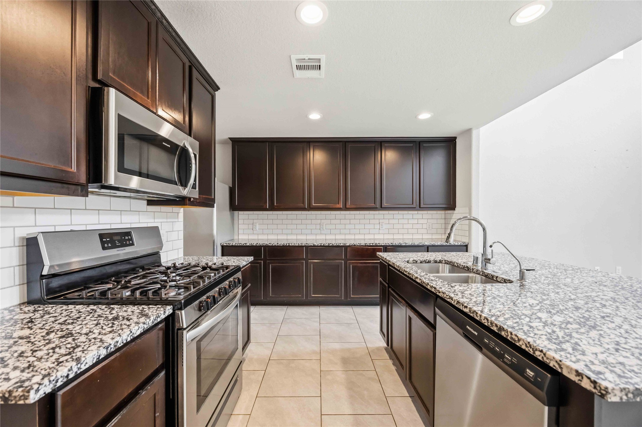 703 Autumn Flats Way Rosharon, TX 77583 - Photo 4 of 18 Prepare to fall in love with this sleek, gourmet kitchen. Fully equipped with a high-quality Frigidaire stainless steel suite, including a gas range, built-in microwave, and dishwasher.Expansive granite countertops and white subway tile backsplash adds a touch of traditional charm and makes for incredibly easy cleanup.