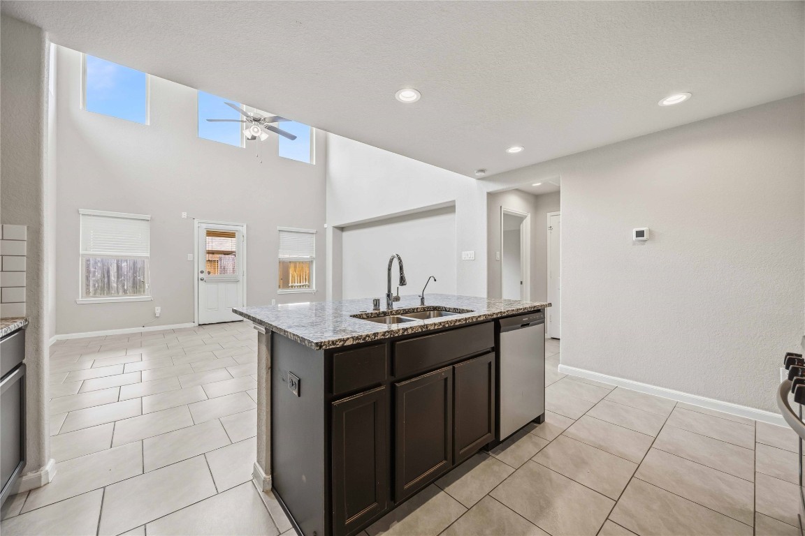 703 Autumn Flats Way Rosharon, TX 77583 - Photo 5 of 18 The oversized kitchen island serves as the home's hub, featuring a double undermount sink, integrated dishwasher, and rich espresso cabinetry for a sleek, uniform look. The upper-tier windows from the living area are visible from the kitchen, ensuring that even the chef enjoys the expansive views and abundant natural light.