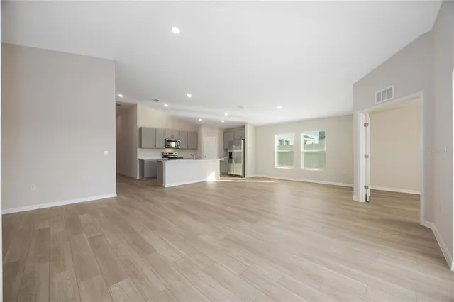 a view of empty room with wooden floor and kitchen