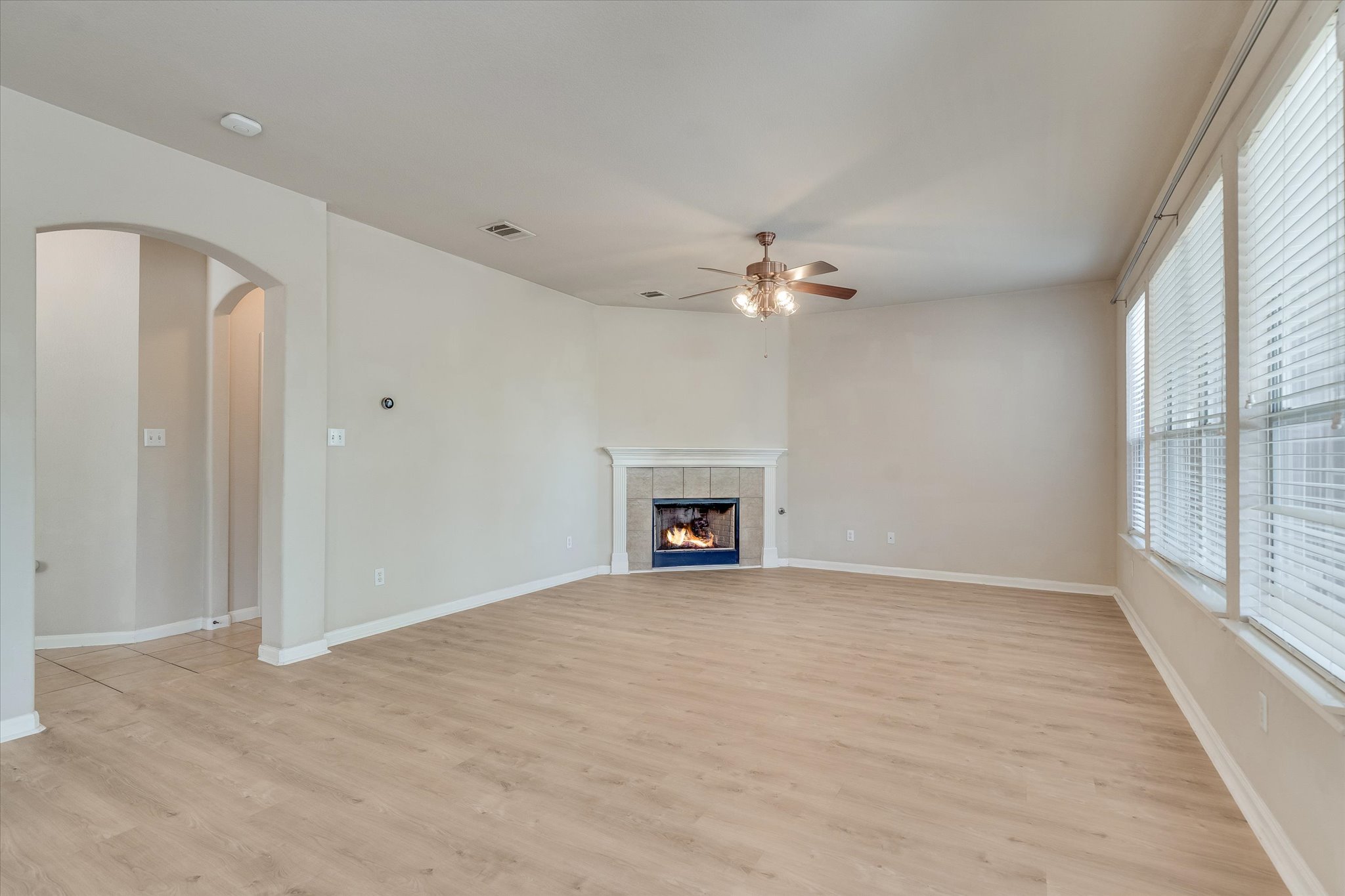 4029 Lake Edge Way Pflugerville, TX 78660 - Photo 7 of 35 Unfurnished living room featuring arched walkways, a tile fireplace, light wood-style flooring, and ceiling fan