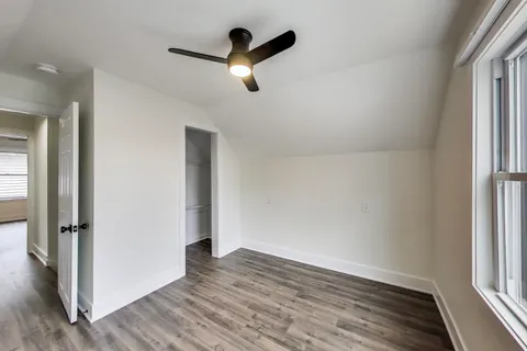 an empty room with wooden floor a ceiling fan and windows