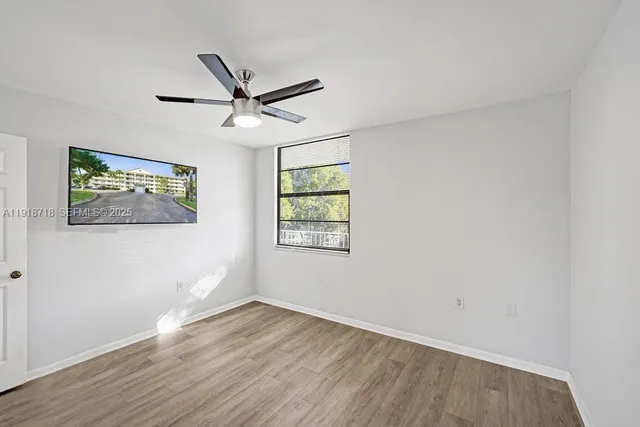 an empty room with wooden floor ceiling fan and windows