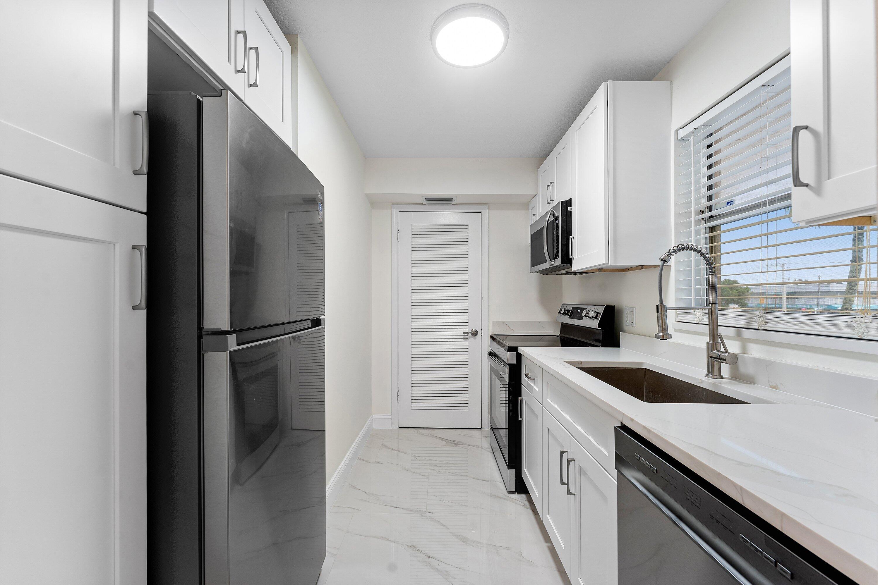 9911 Sandalfoot Boulevard, Unit 113 Boca Raton, FL 33428 - Photo 5 of 19 a kitchen with a sink a refrigerator and cabinets