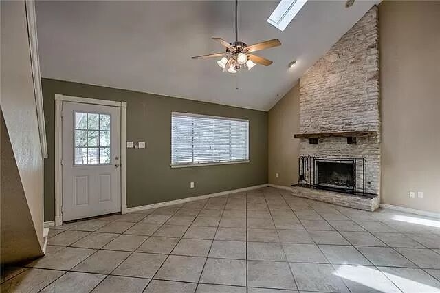 7801 Coldstream Drive Austin, TX 78748 - Photo 1 of 20 Unfurnished living room featuring high vaulted ceiling, light tile patterned floors, a skylight, ceiling fan, and a fireplace