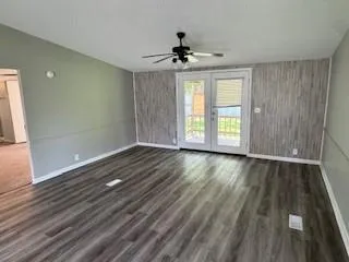 an empty room with wooden floor chandelier fan and windows