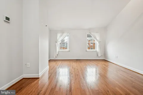 an empty room with wooden floor white walls and windows