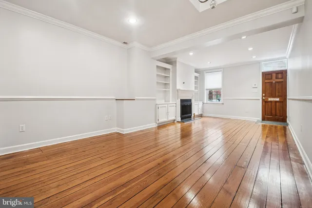 a view of empty room with wooden floor and kitchen