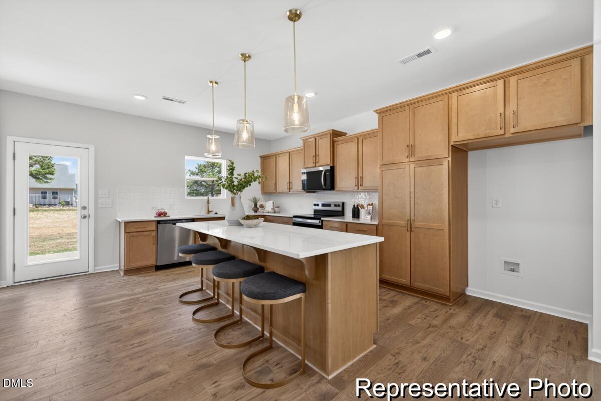 421 Plentiful Way, Unit 111 Benson, NC 27504 - Photo 2 of 27 a kitchen with kitchen island a stove a refrigerator a sink dishwasher with a dining table and chairs with wooden floor