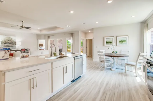 a large kitchen with cabinets a sink dishwasher a dining table and chairs with wooden floor