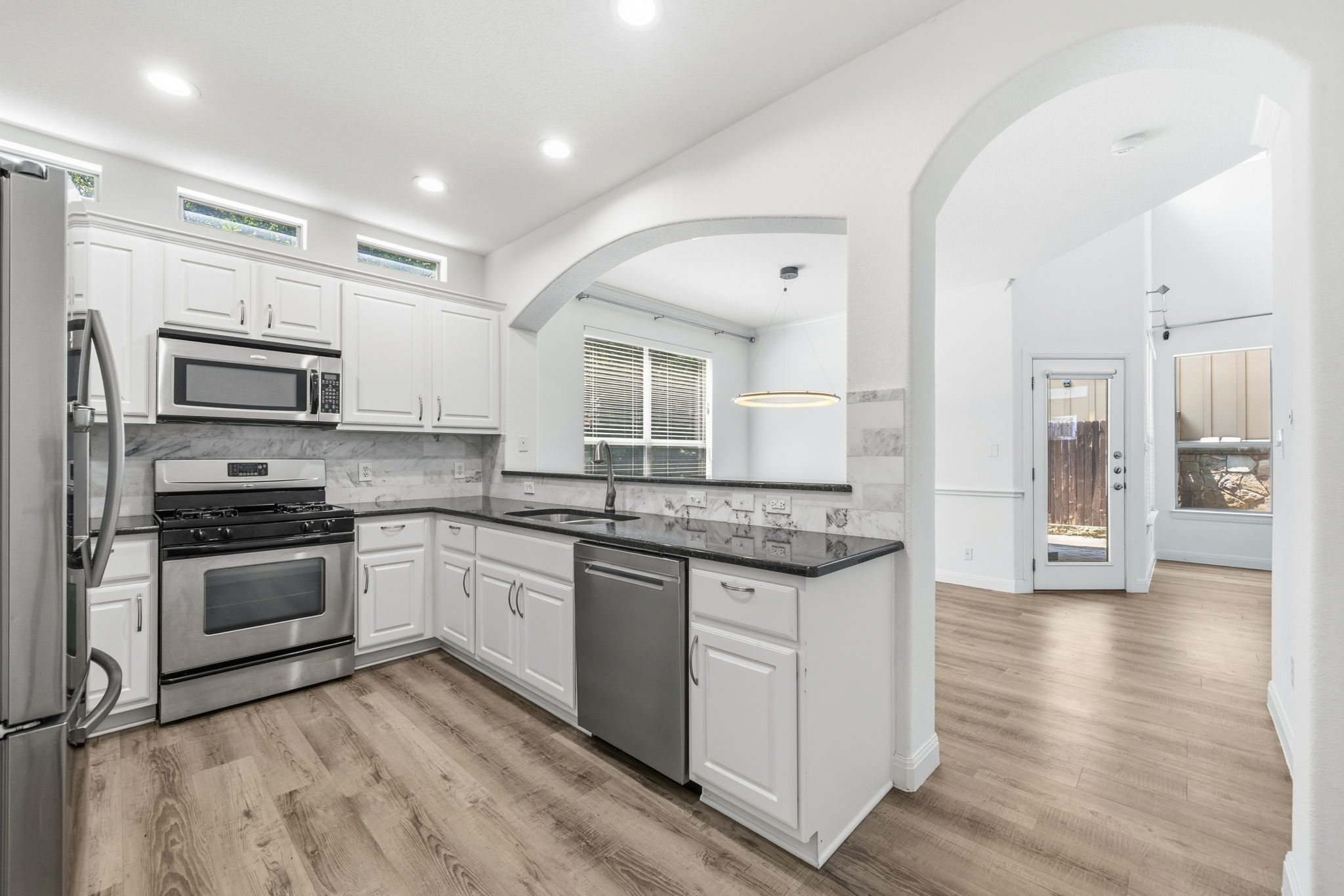6708 Manchaca Road, Unit 4 Austin, TX 78745 - Photo 8 of 25 An arched pass-through highlights this kitchen featuring stainless steel appliances and wood-look flooring.