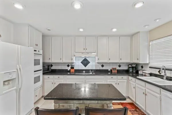 a kitchen with kitchen island granite countertop a sink a stove a refrigerator and white cabinets