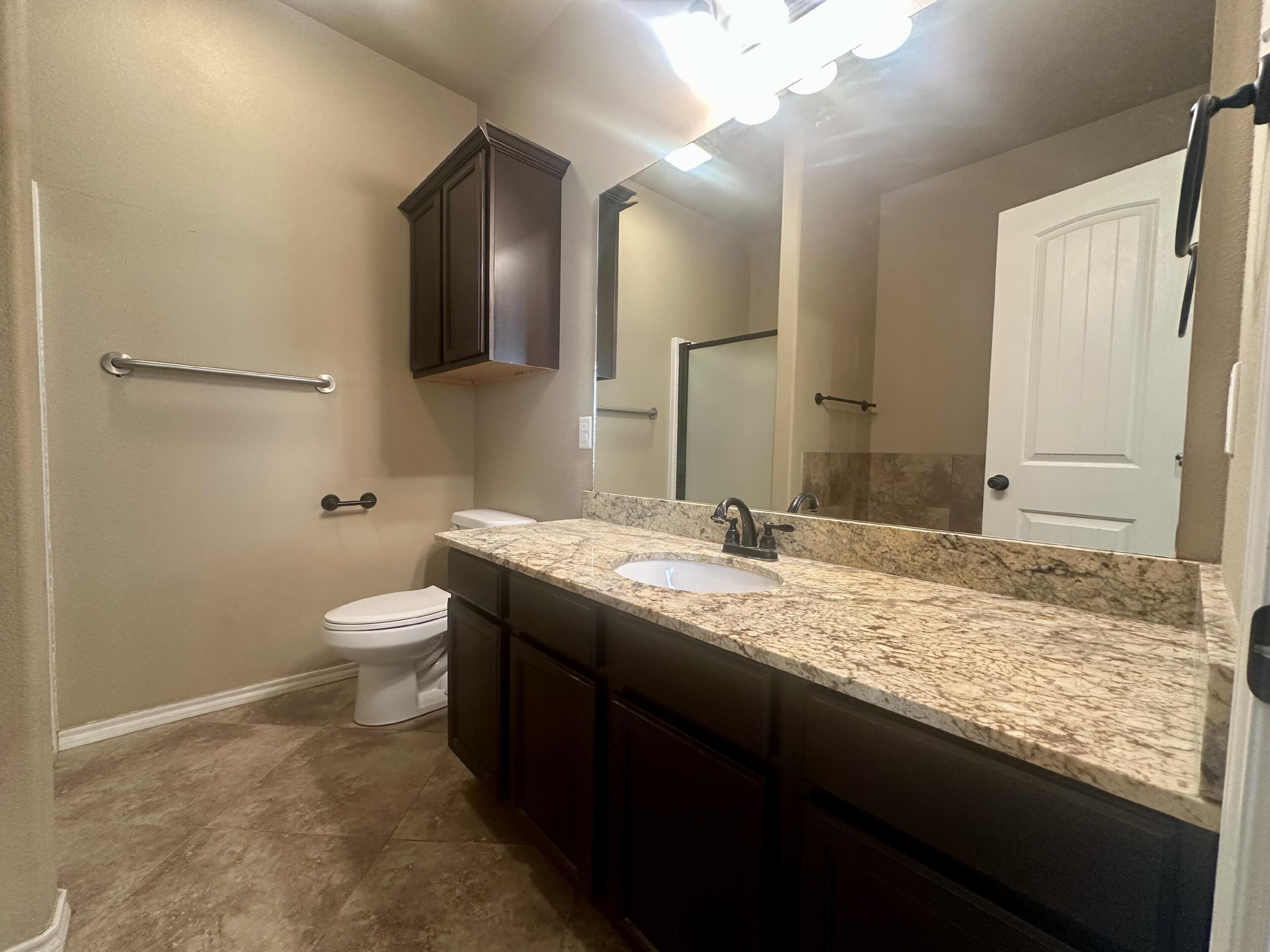 4423 106th Street, Unit A Lubbock, TX 79424 - Photo 14 of 23 a bathroom with a granite countertop sink a toilet and a mirror
