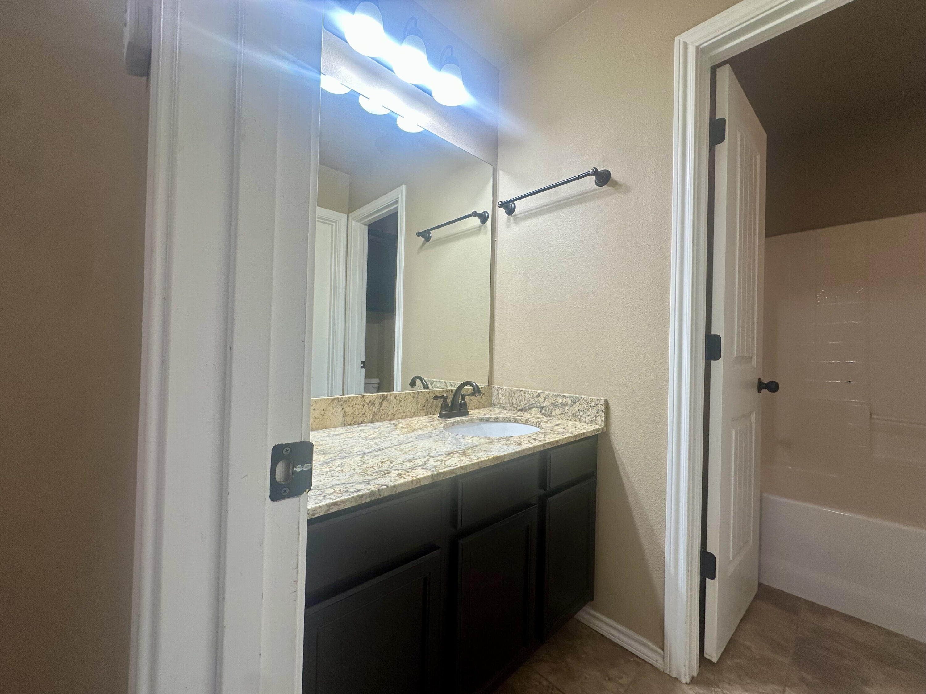 4423 106th Street, Unit A Lubbock, TX 79424 - Photo 21 of 23 a bathroom with a granite countertop sink a mirror and a shower