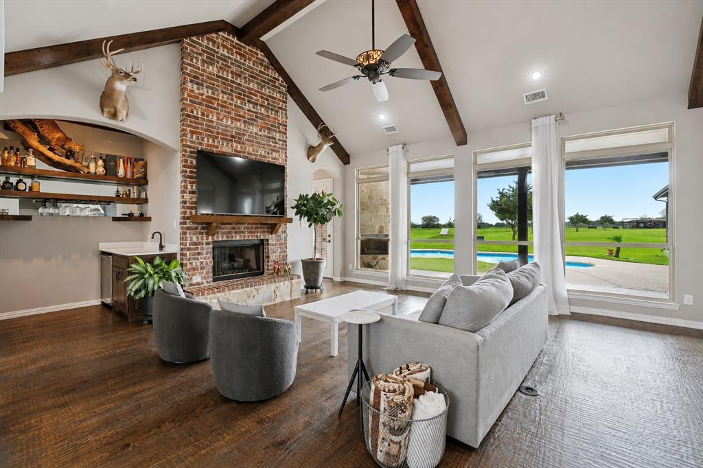 542 Pierce Road Red Oak, TX 75154 - Photo 4 of 27 Vaulted ceiling with exposed wood beams, brick fireplace, built-in wet bar, wood-finish flooring, and multiple large windows overlooking the outdoor pool area